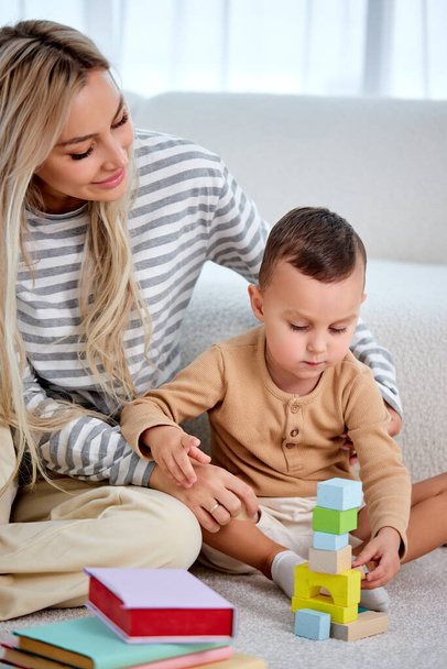 Lovely caucasian mother play with little kid son sit on warm floor, caring mom nanny - Zdjęcie, obraz
