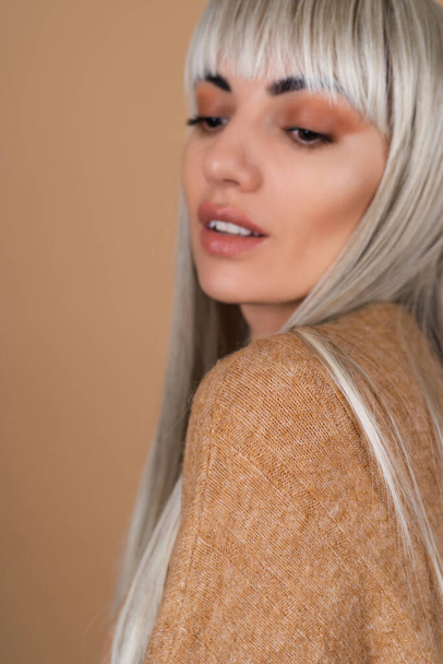 Blondynka z grzywką i brązowy makijaż dzienny w swetrze na beżowym tle zmysłowy portret mody - Zdjęcie, obraz