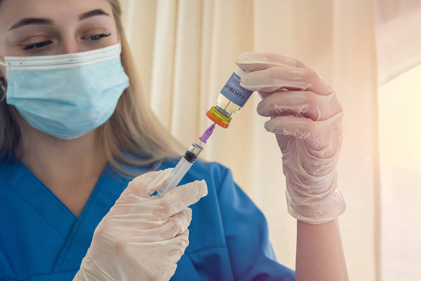 mooie jonge blonde verpleegster met een masker en handschoenen kiest een vaccin voor een patiënt. Geneesmiddelenconcept - Foto, afbeelding