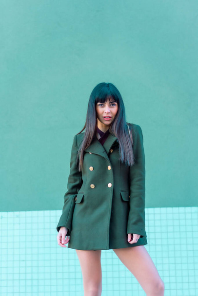 Brunette model in a streetyle on the street with a green jacket. Caucasian pretty a green and blue background - 写真・画像