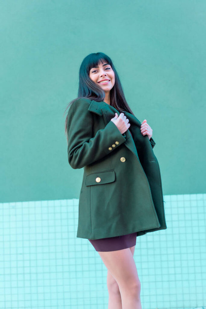 Brunette model smiling in a streetyle in a green jacket. Caucasian pretty a green and blue background - 写真・画像