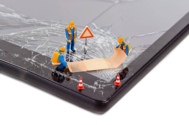 A team of miniature workmen repairing a broken mobile phone tablet touchscreen with a first aid plaster - Photo, Image