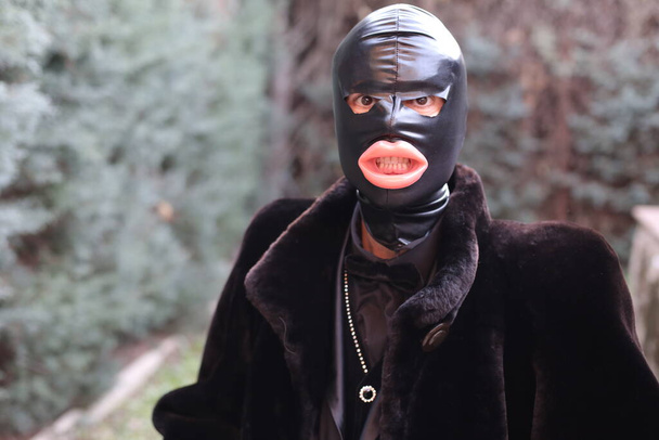 close-up portrait of man in bdsm slave latex mask and fur coat outdoors - Zdjęcie, obraz