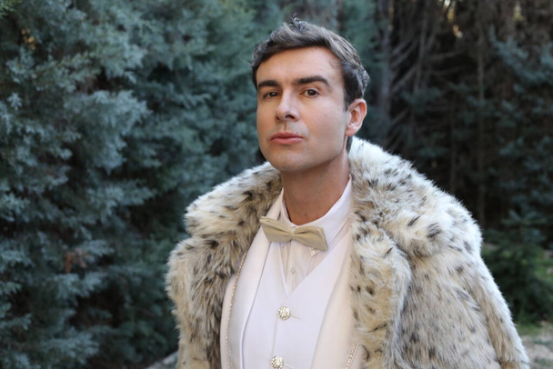 close-up portrait of handsome young man in white suit and snow leopard fur coat outdoors - Photo, Image