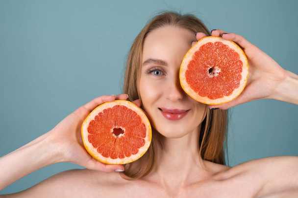 Крупним планом портрет топлес-жінки з ідеальною шкірою і натуральним макіяжем, повними оголеними губами, що тримає свіжий цитрусовий вітамін С грейпфрут
 - Фото, зображення