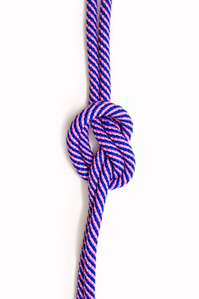 Buntes blau-rosa Seil mit einem Knoten auf weißem Hintergrund. Doppelt starkes Seil mit einem halbengen Knoten in minimalistischem Stil in einem vertikalen Foto. Seil und Freiraum für Text und Werbung - Foto, Bild