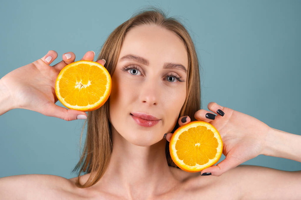 Portrait en gros plan d'une femme seins nus avec une peau parfaite et un maquillage naturel, lèvres entièrement nues, tenant des agrumes frais orange vitamine C - Photo, image