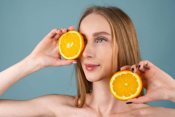 Κοντινό πλάνο πορτραίτο γυμνόστηθας γυναίκας με τέλειο δέρμα και φυσικό make-up, γεμάτα γυμνά χείλη, που περιέχει φρέσκια βιταμίνη C εσπεριδοειδών πορτοκαλί - Φωτογραφία, εικόνα
