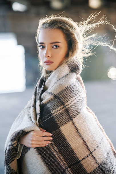 Beautiful young woman portrait wrapped in wool blanket looking to camera on windy sunny day on urban street background - Foto, immagini