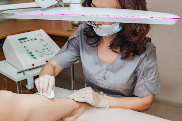 Une femme cosmétologue prépare la peau avant la procédure d'épilation permanente des jambes du client par électroépilation. - Photo, image