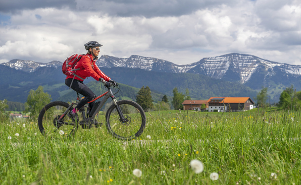 гарна старша жінка їде на електричному гірському велосипеді ранньою весною в районі Альгау (частина Баварських Альп, Німеччина). - Фото, зображення