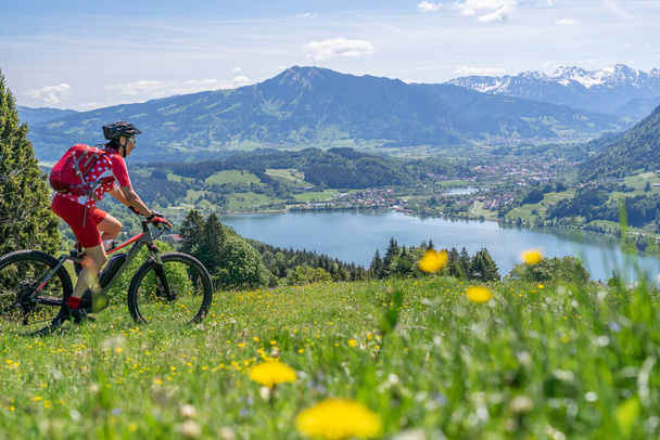 İlkbaharda elektrikli dağ bisikleti süren son sınıf öğrencisi kadın Immenstadt, Allgau, Bavyera, Almanya yakınlarındaki Alpsee dağlarında - Fotoğraf, Görsel