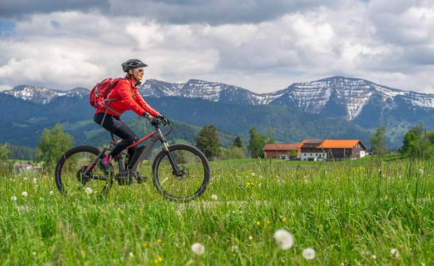 Старша жінка їде на електричному гірському велосипеді ранньою весною в районі Альгау (частина Баварських Альп, Німеччина). - Фото, зображення