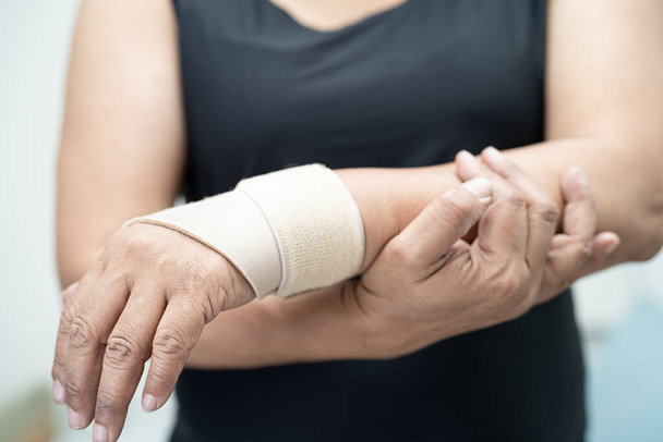 Азіатська середнього віку леді жінка використовувати еластичну пов'язку для лікування де-Керемарний синдром під рукою і пальцем в офісі. - Фото, зображення
