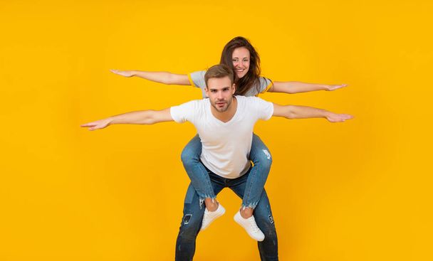 Happy playful girl and guy pretend flying doing piggyback ride yellow background, couple - Foto, Imagem