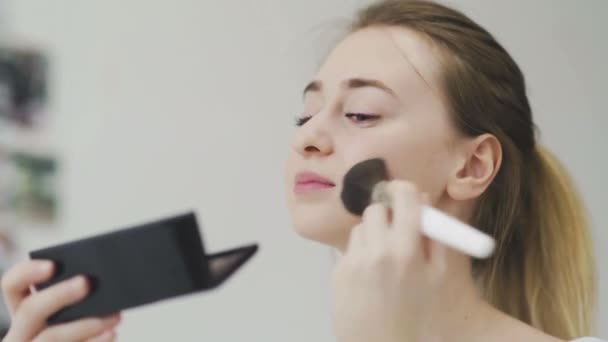 Een jonge vrouw doet haar make-up terwijl ze in een kleine spiegel kijkt - Video