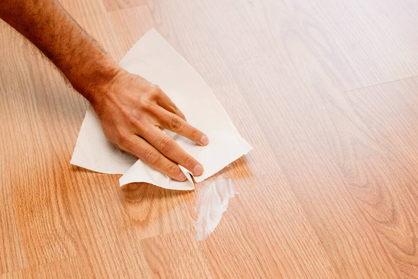 Die Hand eines Mannes wischt mit einem Taschentuch einen weißen Cremefleck auf den Holzboden. - Foto, Bild