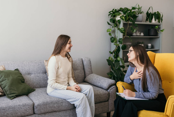 a brunette psychologist and a female patient are sitting in a room and talking. A heartfelt conversation. Solving psychological problems - Photo, Image