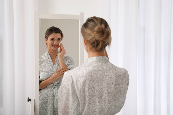 Beautiful young woman cleaning her face near mirror in room - Foto, Imagen
