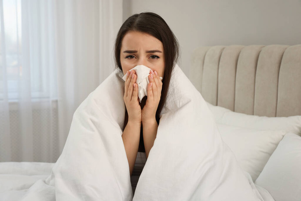Sick young woman with tissue wrapped in blanket at home - Foto, Bild