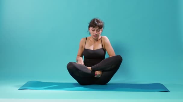Mujer en forma sentada en posición de loto en esterilla de yoga y respiración - Imágenes, Vídeo