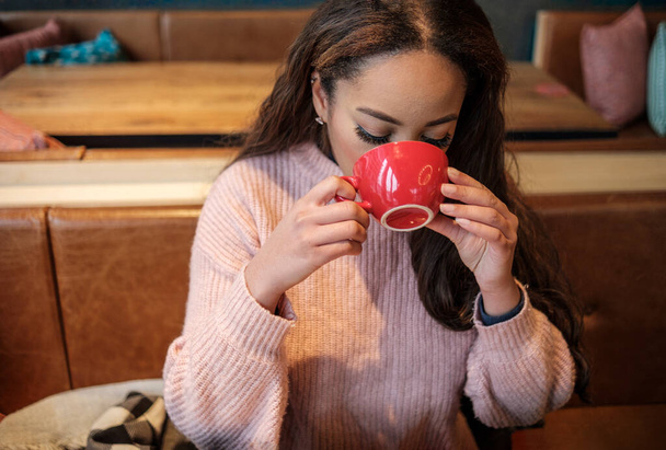 Young black woman is having coffee indoors. She is wearing a wood pullover and she is in a coffee house. - Foto, Bild