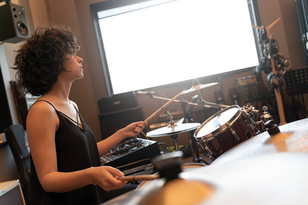 Портрет молодой женщины с вьющимися волосами, играющей на барабанах в студии звукозаписи - Фото, изображение
