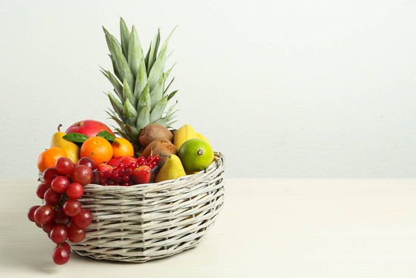 Wicker basket with different fresh fruits on white wooden table. Space for text - Foto, immagini