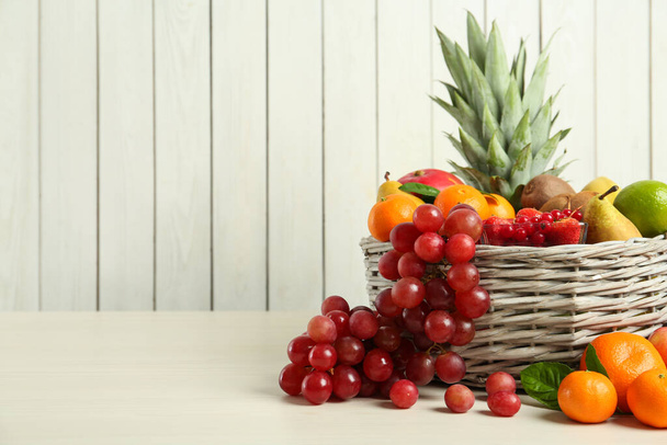 Wiklinowy kosz z różnymi świeżymi owocami na białym drewnianym stole. Miejsce na tekst - Zdjęcie, obraz
