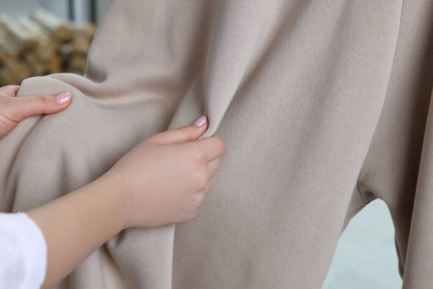 Woman touching clothes made of soft beige fabric indoors, closeup - Fotó, kép