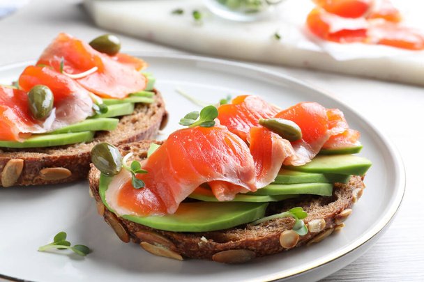 Delicious sandwiches with salmon, avocado and capers on plate, closeup - Foto, Imagem