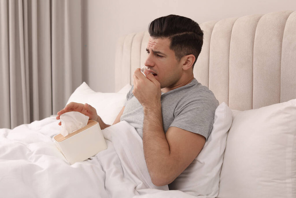 Sick man with box of paper tissues suffering from cold in bed at home - Фото, изображение