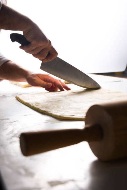 dettaglio sul piano di lavoro in cucina mentre il cuoco taglia la pasta sfoglia con un coltello - Foto, immagini