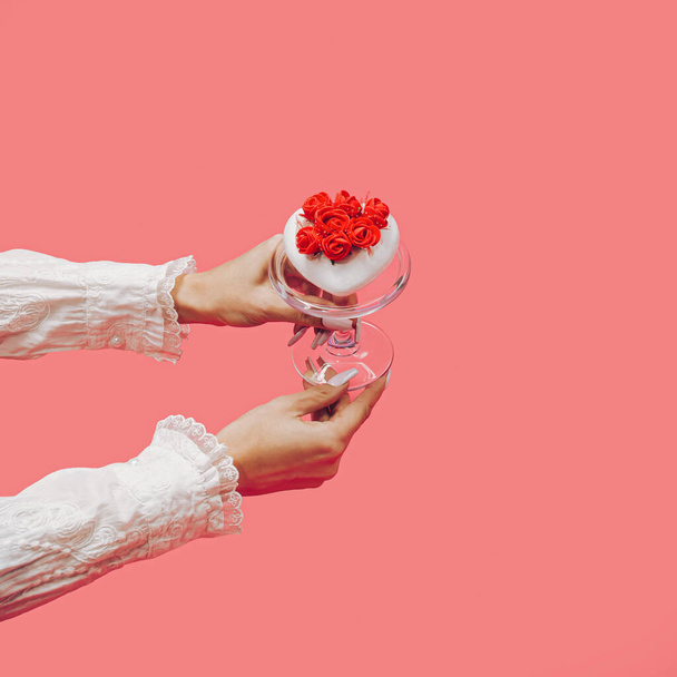 Die Hände einer Frau geben ein rotes Herz auf einem Glasteller. Die schöne Gegenwart. Weißes Herz mit kleinen roten Rosen. Minimal Valentinstag oder Jubiläums-Konzept. Fashion Love Konzept. Liebesdessert. - Foto, Bild