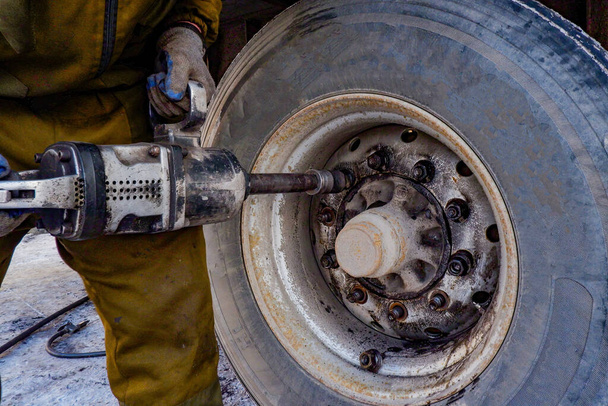 un trabajador de reparación de neumáticos desenrosca las ruedas de un vehículo de servicio pesado con una llave neumática, - Foto, imagen