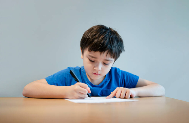 School kind met behulp van zwarte pen tekening of het schrijven van de brief op papier, Jonge jongen doet huiswerk, Kind met pen schrijven notities op papier blad tijdens de les.Leuke leerling doen test, Thuisonderwijs concept - Foto, afbeelding