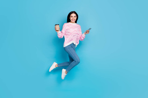 Full length photo of young girl jumper energetic latte espresso use mobile fast connection 4g isolated over blue color background - Фото, зображення
