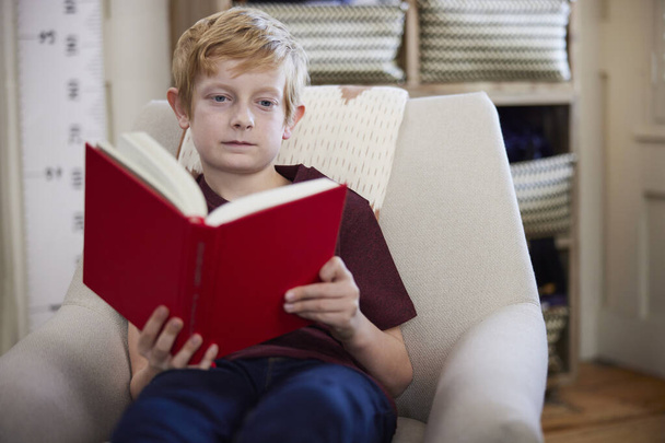 Menino sentado na cadeira no quarto em livro de leitura em casa - Foto, Imagem