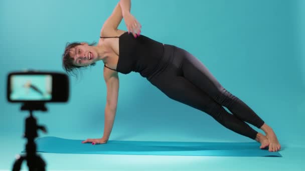 Instructor de yoga filmando ejercicio de estiramiento en cámara en estudio - Imágenes, Vídeo