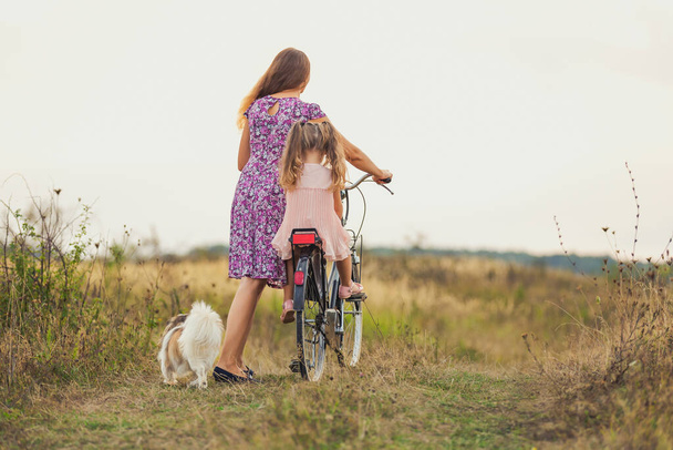 mother and daughter walking with a bicycle and a dog - Foto, imagen