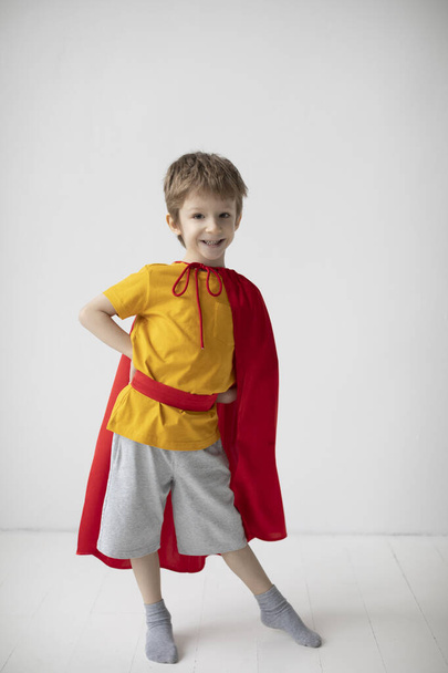 Portrait of a smiling little boy dressed like superhero standing alongside the white wall, having fun at home. - Photo, Image