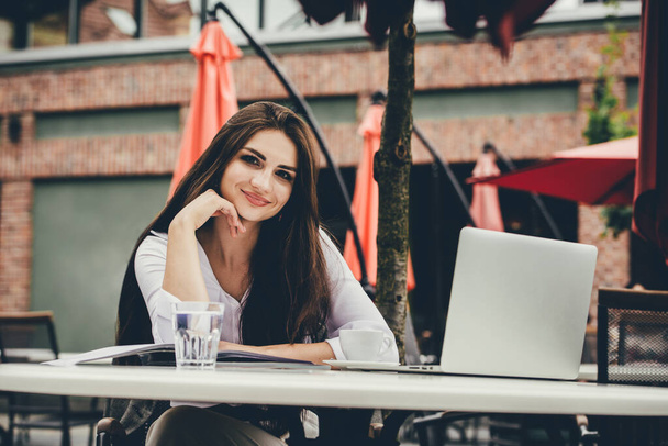 Młoda freelancerka używająca laptopa siedząca przy stoliku. Uśmiechnięta kobieta pracująca online lub studiująca i ucząca się podczas korzystania z notebooka. - Zdjęcie, obraz