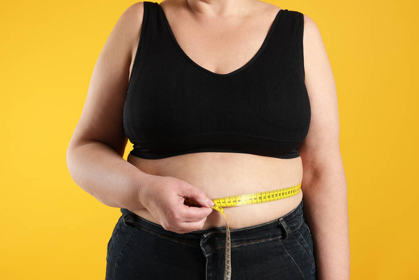 Overweight woman measuring waist with tape on orange background, closeup - Fotoğraf, Görsel