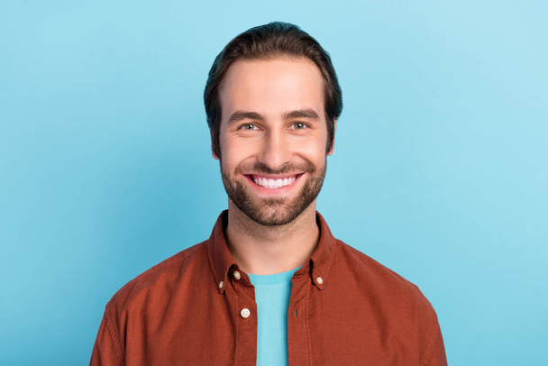 Portrait of young smiling positive guy in brown shirt laughing with perfect white veneer teeth isolated on blue color background - Фото, изображение