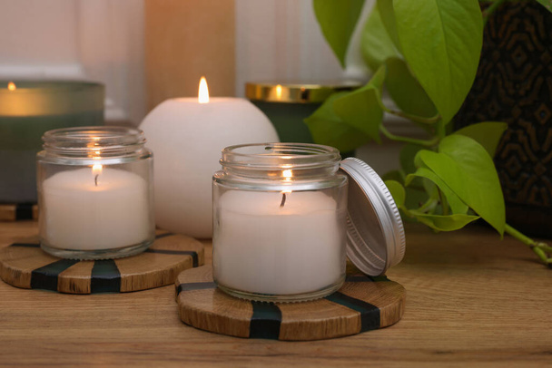 Burning candles and houseplant on wooden table indoors, closeup - Foto, afbeelding