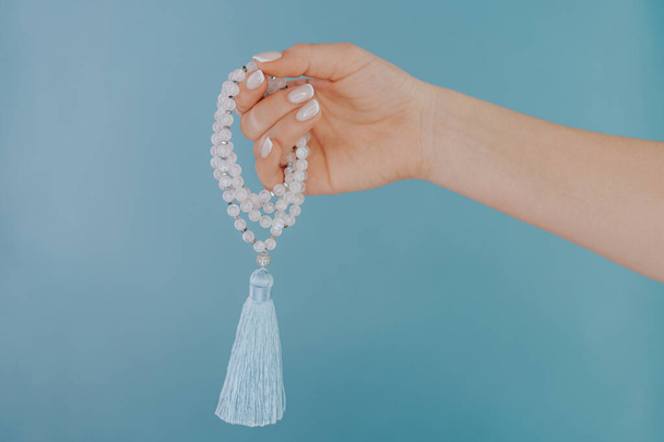 Moon stone mala beads in female hand on blue background. Gemstone strand used for keeping count during mantra meditations. Spirituality, religion, God concept. - 写真・画像