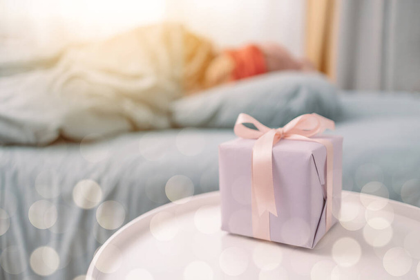 Ημέρα των γυναικών. Γυναίκα κοιμάται στο κρεβάτι κοντά σε κουτί δώρου. Χριστούγεννα, Πρωτοχρονιά, Ημέρα του Αγίου Βαλεντίνου και την έννοια των γενεθλίων - Φωτογραφία, εικόνα