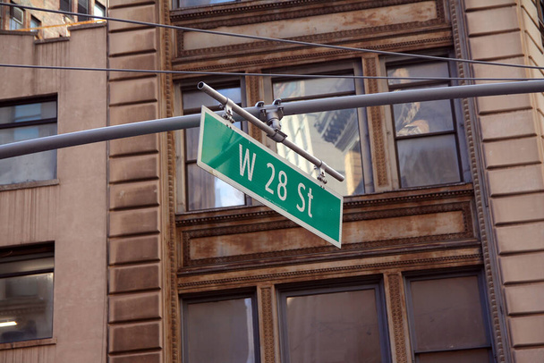 Grünes großes West-28th-Street-Schild hängt an einem Bogenmast in den Straßen von Midtown Manhattan in New York City - Foto, Bild