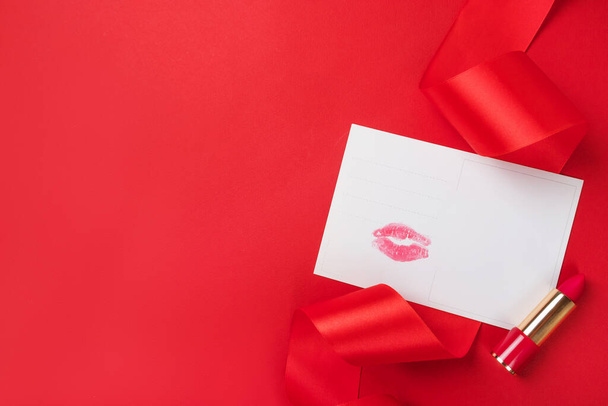 Valentýn flatlay s polibkem tisk pohlednice, rtěnka a lesklé červené stuhy izolované na červeném pozadí. - Fotografie, Obrázek