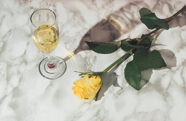 Minimal vintage style concept with wine glass and yellow rose flower on marble table. Retro Valentine's day party concept. Modern aesthetic. - Фото, изображение